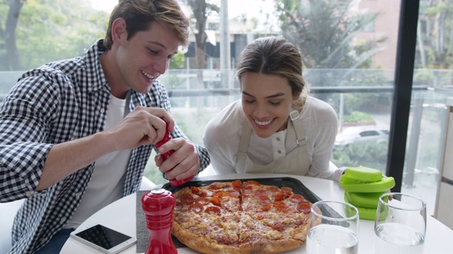 爱的女人烤一个美味的披萨在桌子上，同时看着伴侣微笑视频下载