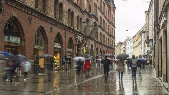 德国慕尼黑下着雨，人们走在购物街上，但游客仍然撑着伞观光视频下载