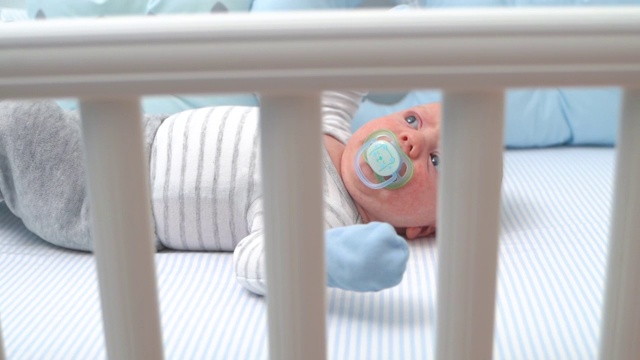 可爱的小男孩躺在他的婴儿床吮吸奶嘴中镜头俯视图特写慢动作视频下载