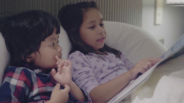 姐姐在他们的公寓里给小男孩读童话故事视频素材