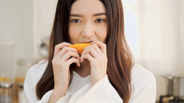 年轻美丽的亚洲女人在厨房喝橙汁视频素材