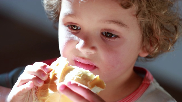 小男孩在吃三明治，小男孩咬了一口带有火腿和奶酪的面包视频素材