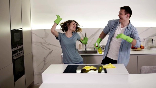 快乐的年轻夫妇在厨房跳舞都在绿色橡胶手套有乐趣的清扫日在单间公寓。现代青年，人与家务观念视频素材