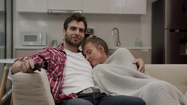 近距离的爱的男人拥抱美丽的女人在他旁边的沙发上看电视视频素材