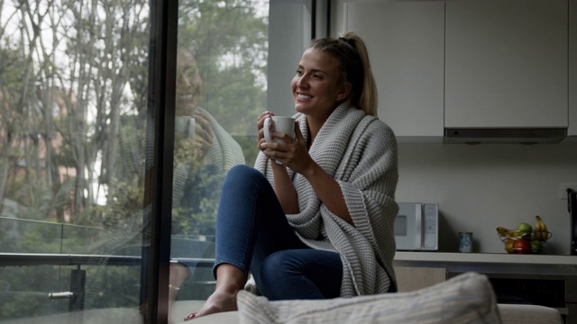 体贴的女人在一个寒冷的日子里在家喝茶，看着窗户视频下载
