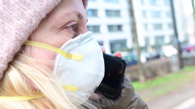 一名妇女在大街上戴着防护面具和手机通话。在德国柏林的大街上走着一群不认识的人。视频素材