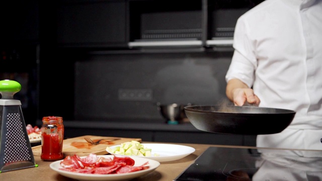 在餐厅厨房里，一名面目全的厨师在煎菜时把蔬菜扔进锅里，用慢镜头追踪视频素材