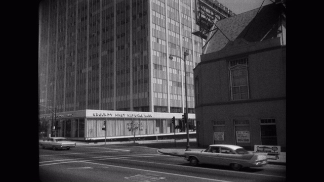 20世纪60年代——美国加州洛杉矶威尔希尔大道，旅行者保险大楼前的街道上行驶的汽车倾斜镜头视频素材
