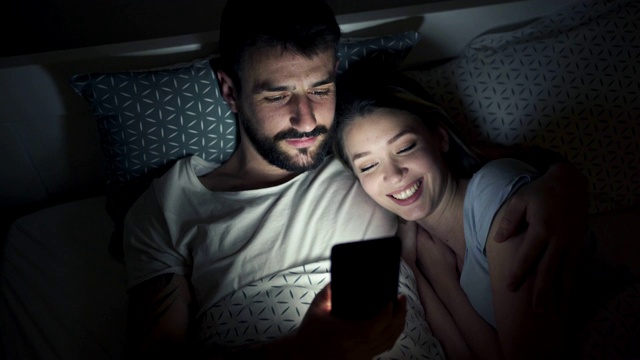 幸福的夫妇在床上浏览社交媒体视频下载