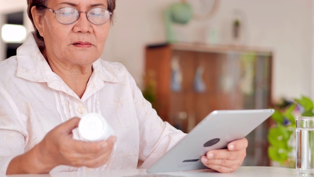 亚洲老年妇女患者与医生视频聊天如何在家里的平板电脑上服药。采购产品技术，医疗保健，创新，福利，护理，力量，健康和活力，医疗，教育，退休，医疗保健和医药视频下载
