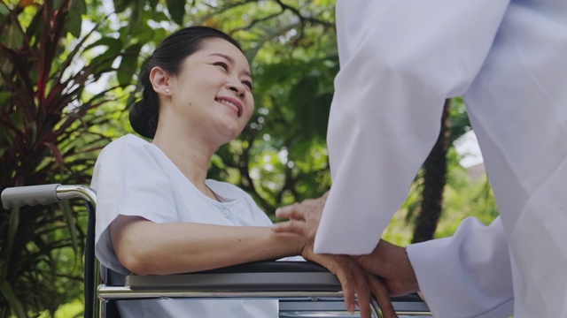 关怀的手，亚洲医生在轮椅与花园背景高级妇女的手。幸福的微笑。视频素材