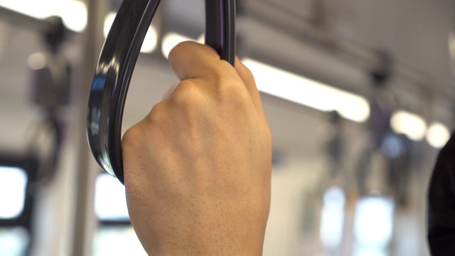 在公共交通中，一个年轻人在地铁里抓着扶手。把手带放在焦点上视频素材