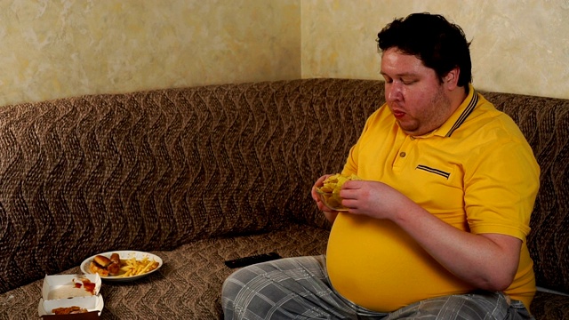 一个胖子坐在家里的沙发上，看电视，吃快餐视频素材