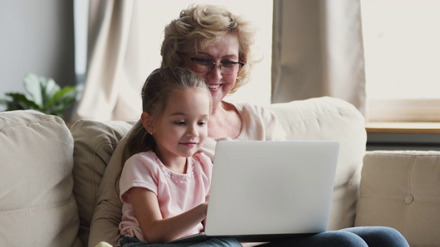 微笑的老祖母和孙女一起在沙发上使用笔记本电脑视频素材