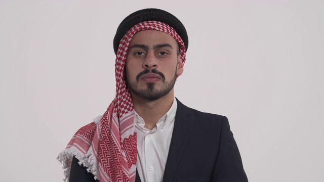一个阿拉伯年轻的自信男子的特写镜头在传统的shemagh看着相机。孤立，在白色背景上。换焦镜头视频下载