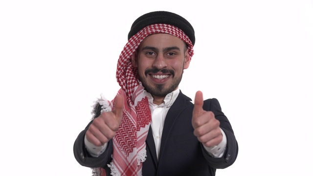 年轻英俊的阿拉伯男子穿着keffiyeh表示幸福(孤立在白色)显示大拇指。真正的情感。肢体语言的概念视频素材