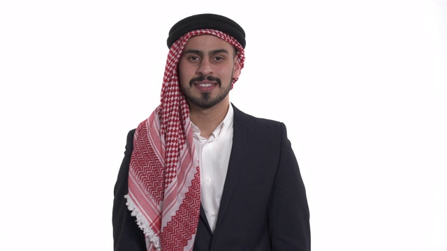 这是一幅正面的阿拉伯青年男子的肖像，他看着镜头，微笑着触摸自己的胸部。孤立，在白色背景上视频下载