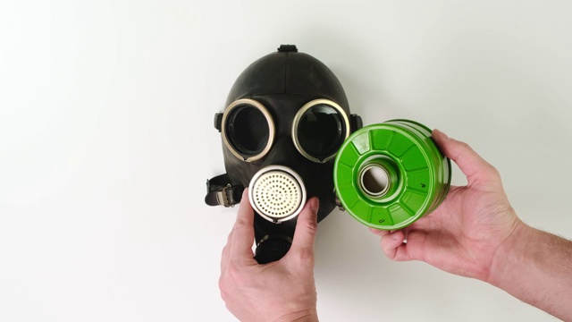 男性双手检查防毒面具上的绿色过滤器，白色背景。视频下载