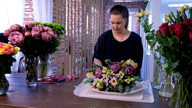 花店女工作人员在花店用白纸包装大花束。视频下载