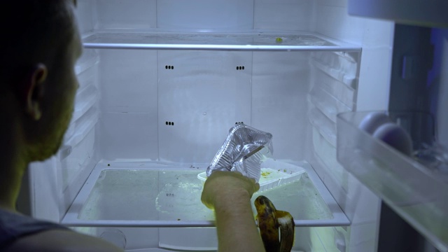 在冰箱里找食物的人。一个在空荡荡的冰箱架子上找吃的东西的人。视频下载
