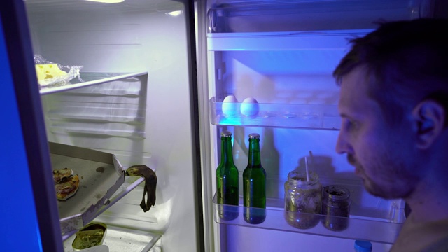 在冰箱里找食物的人。一个没刮胡子的家伙从冰箱里拿了披萨和啤酒。视频下载