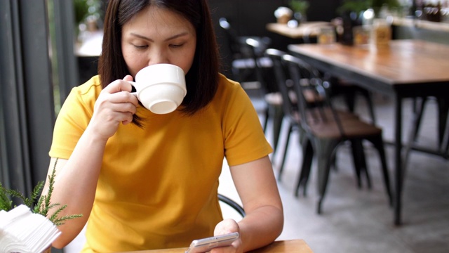 女人用手机，在咖啡馆喝咖啡视频素材