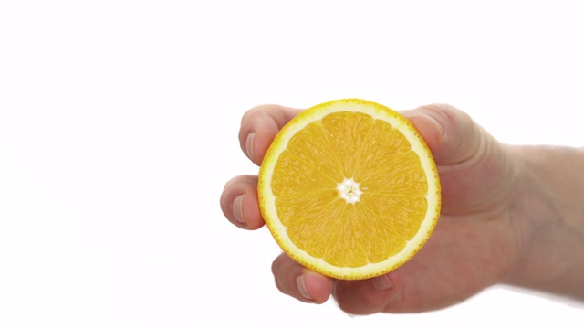 特写镜头:一个不认识的人在挤半颗熟透多汁的橙子。柑橘汁滴下来。孤立，在白色背景上视频素材