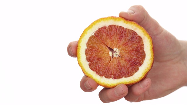 特写镜头:一个面目全非的男人挤着半块血橙。新鲜的柑橘汁滴落下来。孤立，在白色背景上视频素材