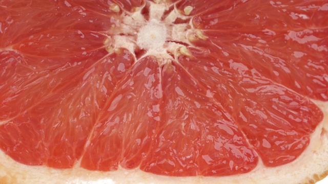 一个成熟多汁的葡萄柚片被滚动和挤压的微距镜头。新鲜的柑橘汁滴落下来。孤立，在白色背景上视频素材
