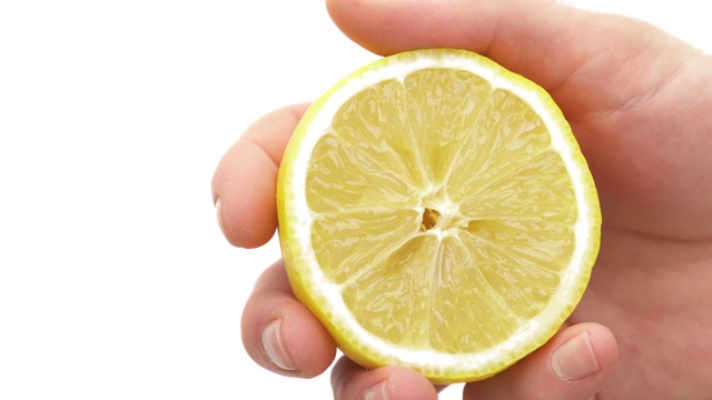 新鲜的柑橘汁从挤在一起的柠檬上滴下来。男性手挤压柑橘类水果的特写。孤立，在白色背景上视频素材
