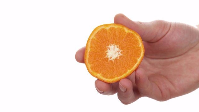 近距离的微距镜头，男性手握和挤压一半成熟多汁的克利奥帕特拉柑橘。柑橘汁滴下来。孤立，在白色背景，复制空间拍摄视频素材