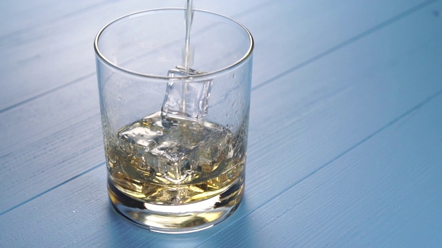 将纯麦芽威士忌和可乐倒入一个蓝色木质背景上有冰块的玻璃杯中视频素材