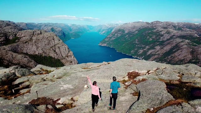 一架无人机飞越吕瑟峡湾，在布道石地区，挪威。一个穿着蓝色衬衫的男人走在峡湾边上的岩石上。徒步旅行的补救办法，给你很多自由。视频下载