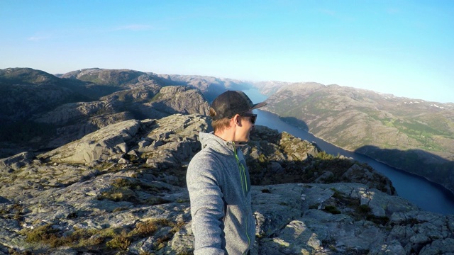 一个男人站在挪威布道石边上。他在欣赏风景。大自然的美。危险的位置。吕瑟峡湾跟在他后面，往大陆深处去。自由和冒险。视频下载