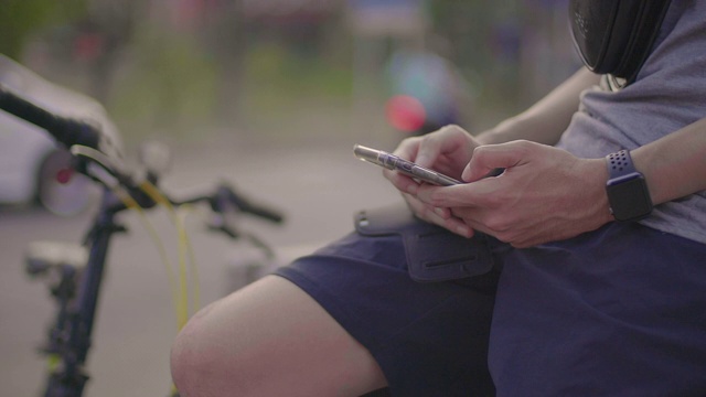 一名亚洲男子骑完自行车后正坐在手机上。视频素材