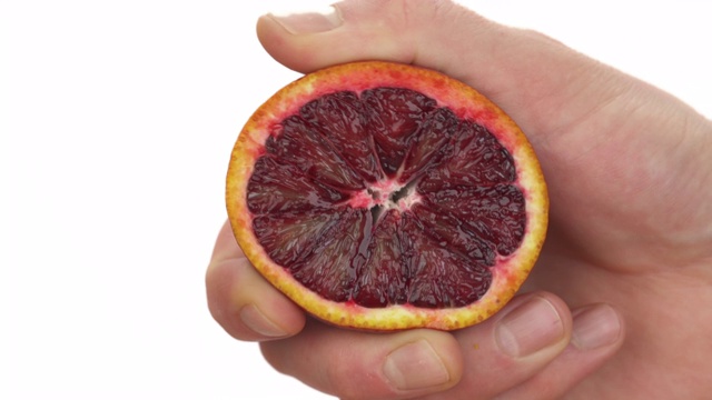 特写镜头:一个不认识的人在挤半块熟透多汁的血橙。新鲜的柑橘汁滴落下来。孤立，在白色背景上视频素材