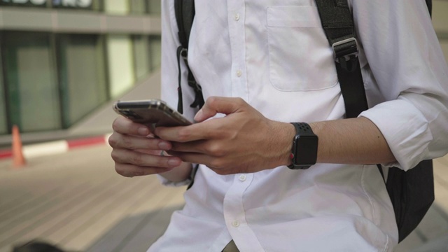 一名穿着衬衫的年轻亚洲男子在城市里使用智能手机视频素材