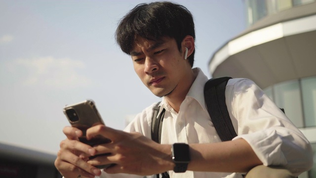 一名穿着衬衫的年轻亚洲男子在城市里使用智能手机视频素材