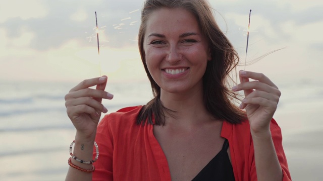 美丽的年轻女子在海滩上微笑着玩烟花。视频素材