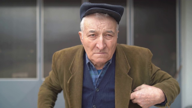 肖像老人退休前视图环顾四周，独自站在户外，穿着夹克和帽子视频下载