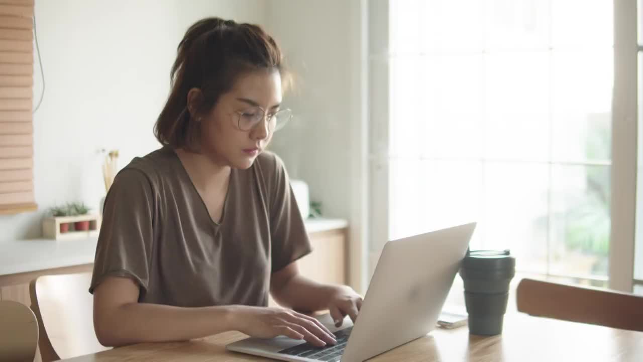 一位亚洲女性在家里使用笔记本电脑时遇到了困难。视频下载