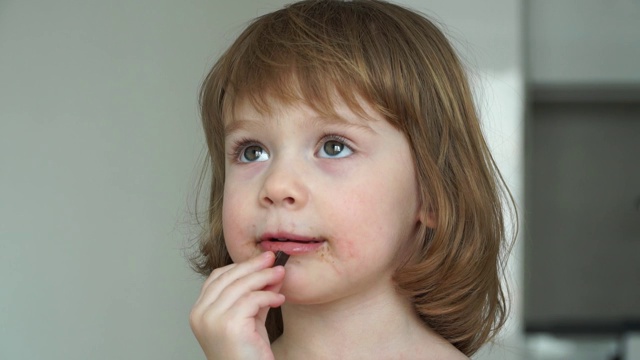 白人滑稽女孩的肖像3岁的女孩吃巧克力大胃口。孩子被巧克力弄脏了。视频素材