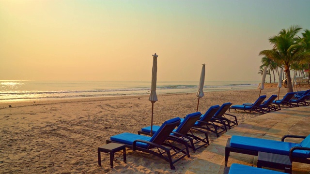 带伞椅的沙滩上有棕榈树和沙滩在日出时间视频下载