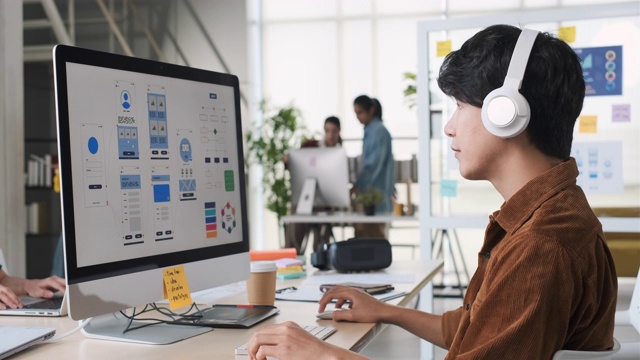年轻的亚洲开发者，与创意团队在现代办公室的电脑桌面上编写手机游戏应用程序。Ux UI设计机构开发视频素材