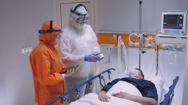 慢镜头:穿着防护服的护士测量冠状病毒患者的体温，并咨询领先医生-宽镜头。拍摄于5K R3D视频素材