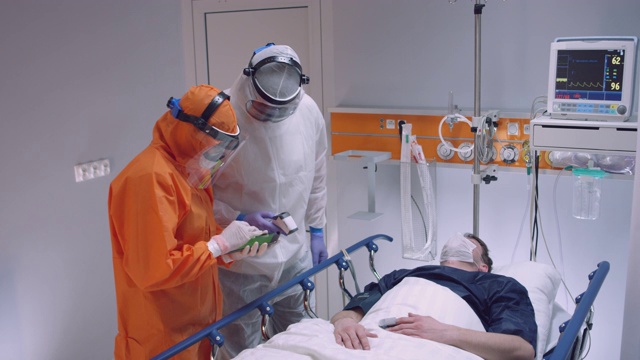 慢镜头:穿着防护服的护士测量冠状病毒患者的体温，并咨询领先医生-宽镜头。拍摄于5K R3D视频素材