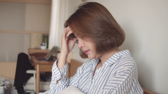 一个亚洲女人得了流感，坐在床上用纸巾打喷嚏视频素材