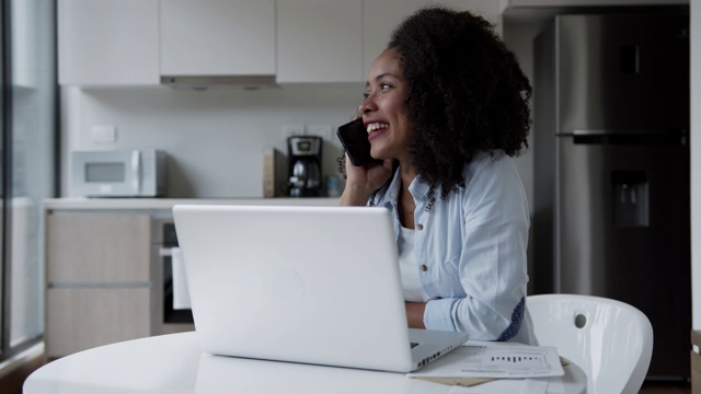 黑人年轻女子工作在家里使用笔记本电脑和接听电话看起来很高兴视频素材