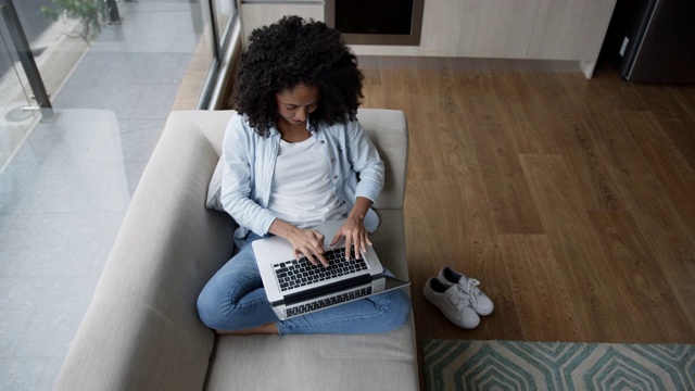 黑人年轻女子在家休息在沙发上用笔记本电脑工作视频素材