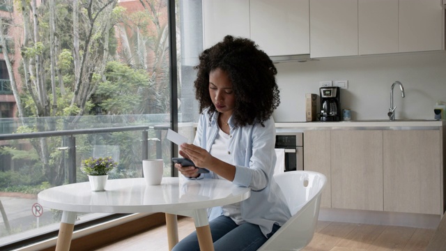 黑人年轻女性在家里用智能手机和信用卡做网上银行，喝着咖啡视频素材